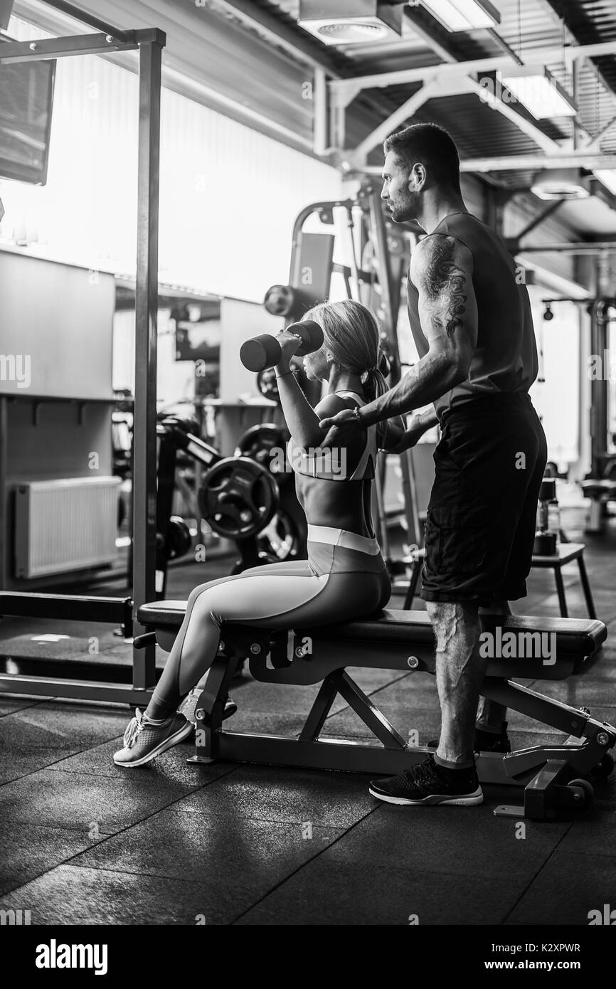 Sporty girl doing weight exercises with assistance of her personal