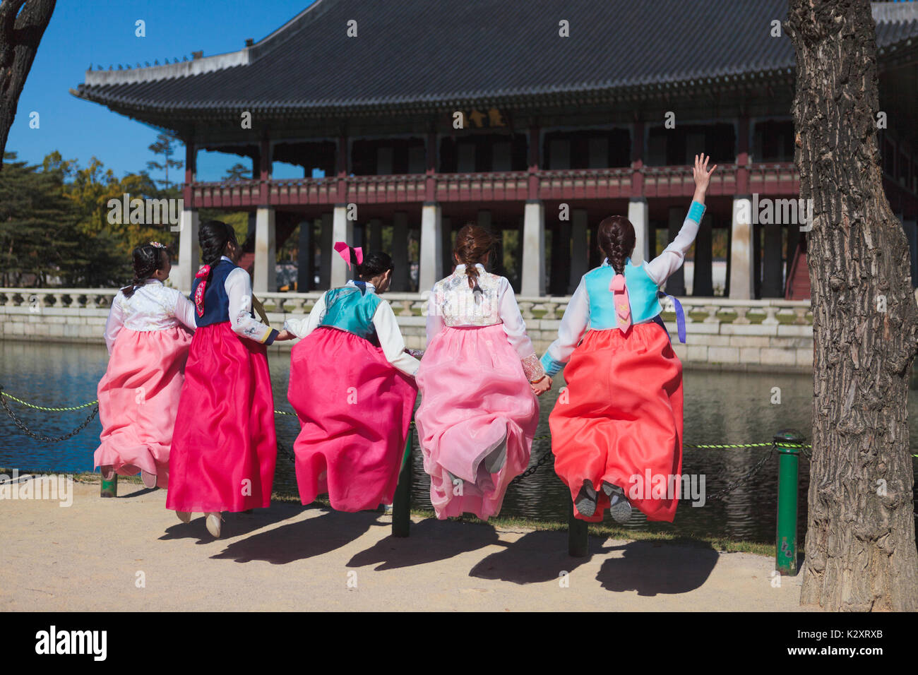 Korean young women wear national costume Hanbok and jump with happy faces and waves hands near Gyeonghoeru, October 30, Seoul, Korea Stock Photo
