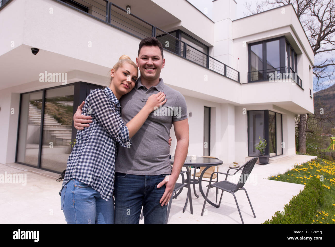 Portrait of a happy young couple hugging in front of their new luxury ...
