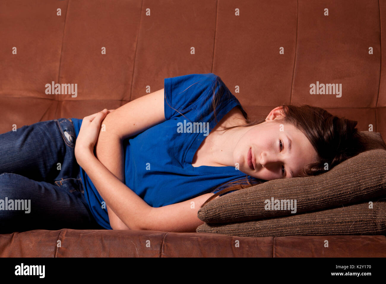 Young teenage girl holding stomach with an illness lying on a couch. Stock Photo
