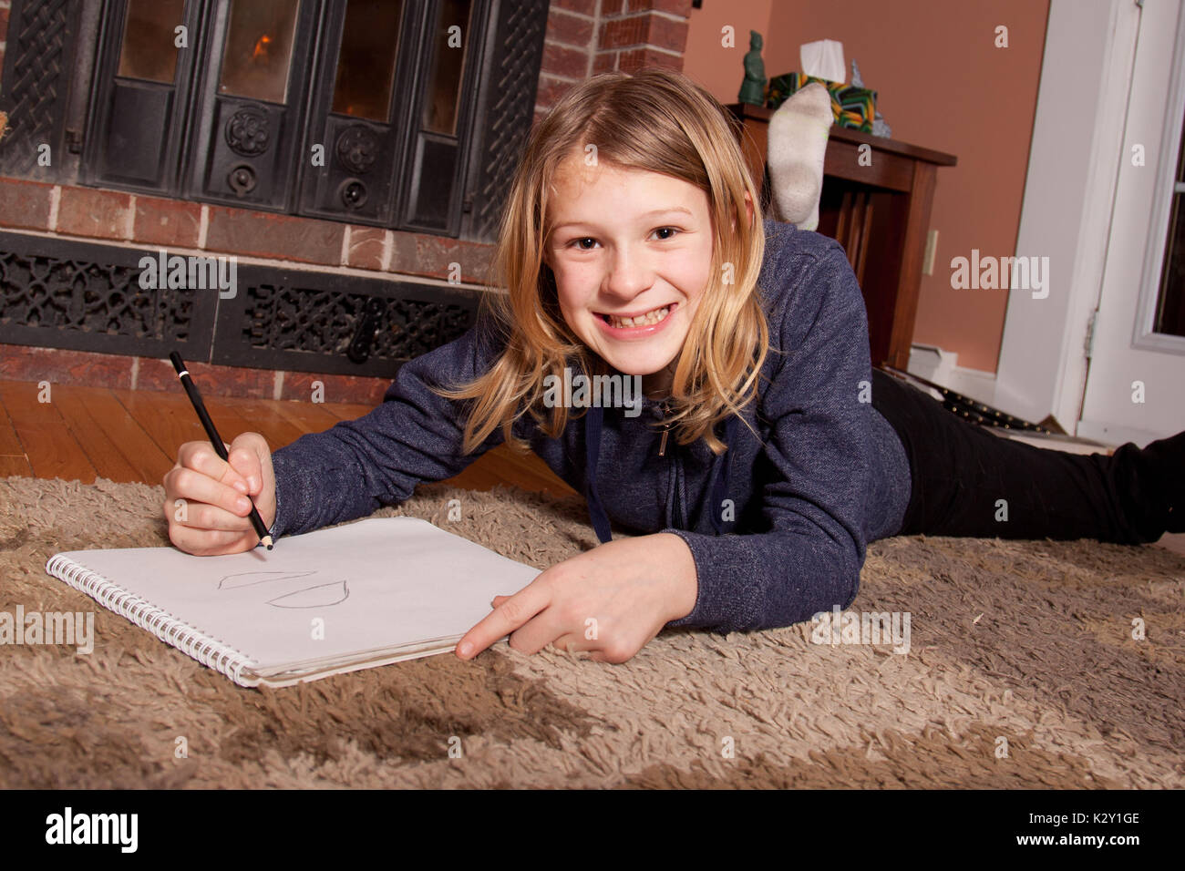 Young girl lying on home floor smiling while drawing pictures Stock ...
