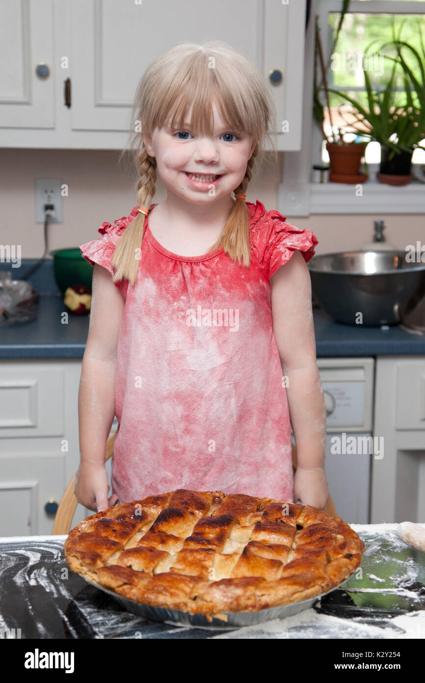 Smiling young girl covered in flour in kitchen with freshly baked pie. Stock Photo
