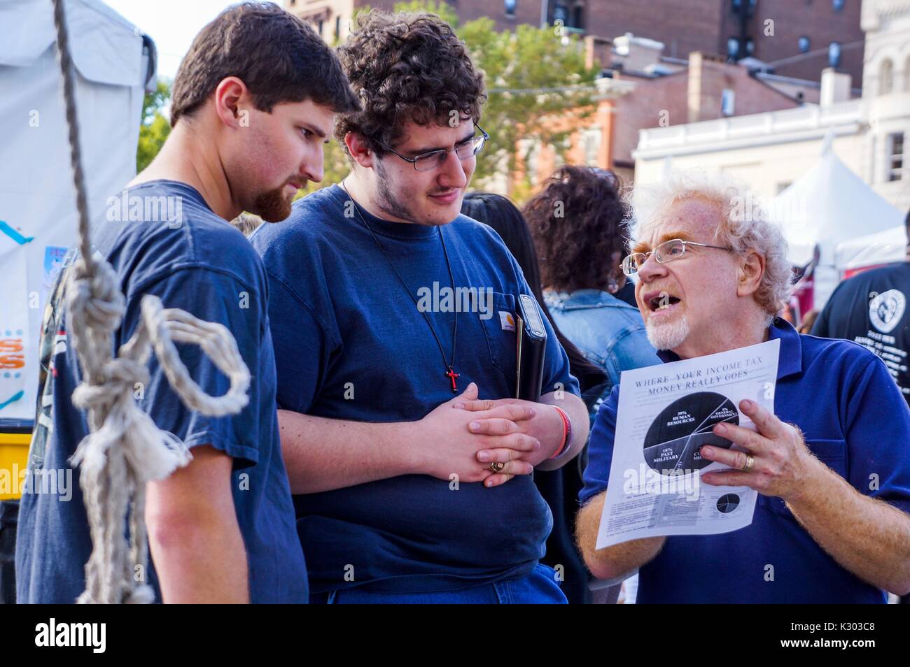An older man with glasses reads from a flyer about income taxes to two young men wearing crosses and holding bibles, during Baltimore Book Festival, Baltimore, Maryland, September, 2013. Courtesy Eric Chen. Stock Photo