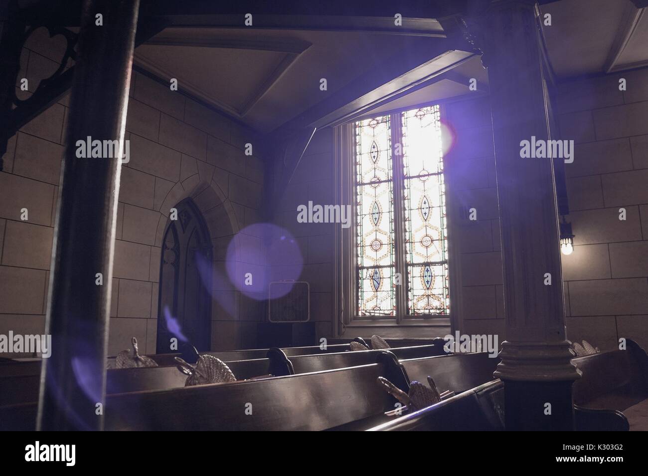 Sun filters through the stained glass of an old church, creating shadows on the pews with woven fans in their holders, Baltimore, Maryland, September, 2013. Stock Photo