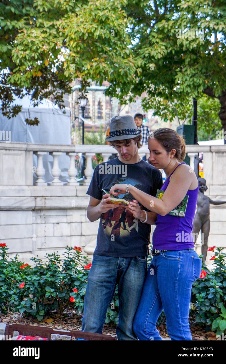 A young couple look at an used book at a vendor stand outside in a park in Mount Vernon at the Baltimore Book Festival, Baltimore, Maryland, 2013. Stock Photo