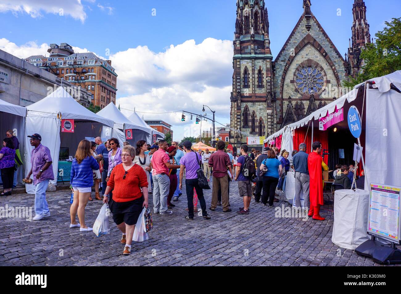 A crowd of people explore vendor tents on a brick path with a church with stained glass windows in the background at the Baltimore Book Festival, Baltimore, Maryland, September, 2013. Stock Photo