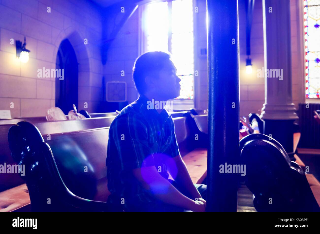 A young man sitting on a pew in a well lit church with stained glass windows at the Baltimore Book Festival, Baltimore, Maryland, September, 2013. Stock Photo