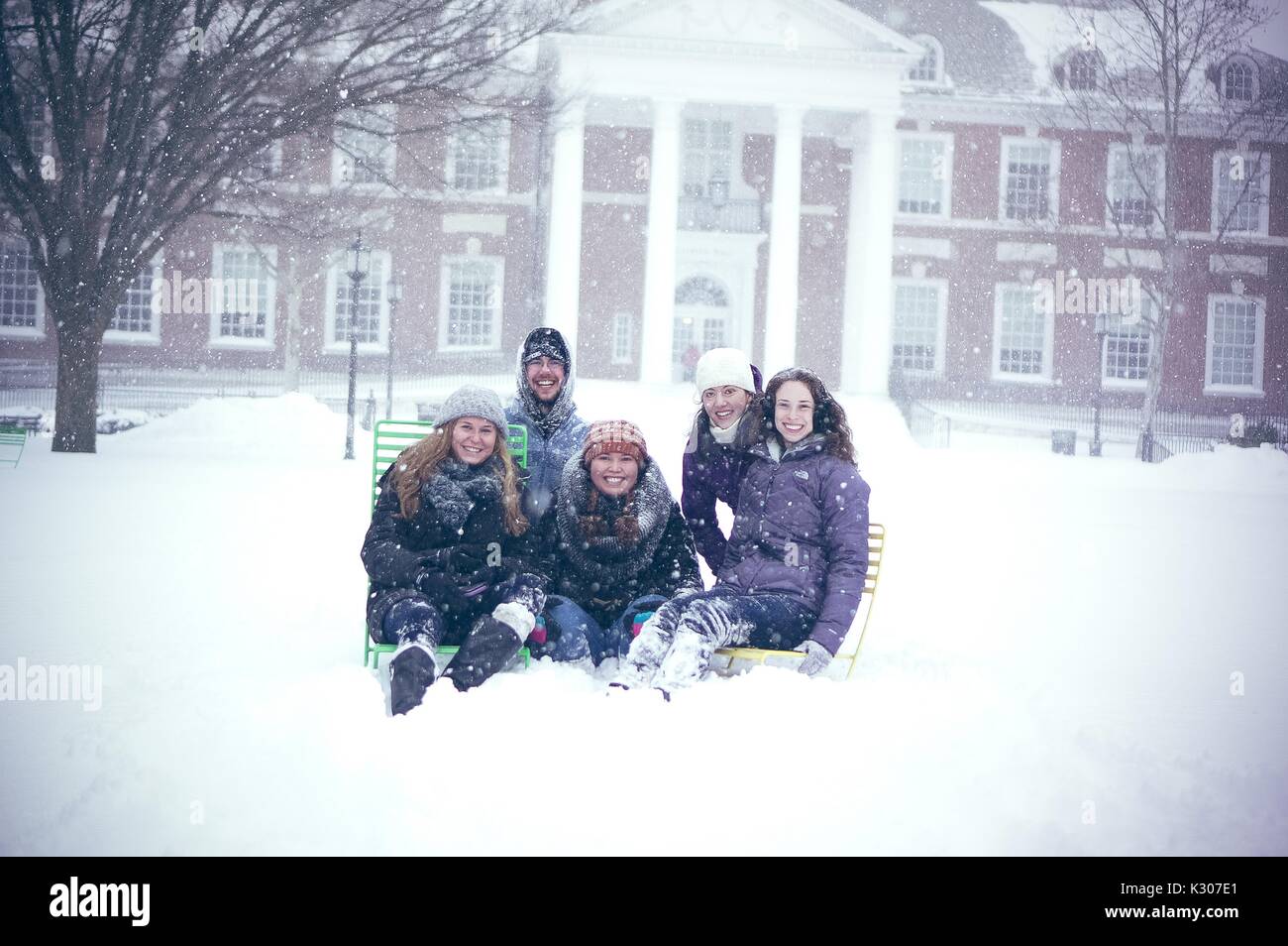 Four female students and one male student sit together on colorful lawn chairs posing for their photo on the snowy quad in front of Gilman Hall, on a snow day at Johns Hopkins University, Baltimore, Maryland, 2016. Stock Photo