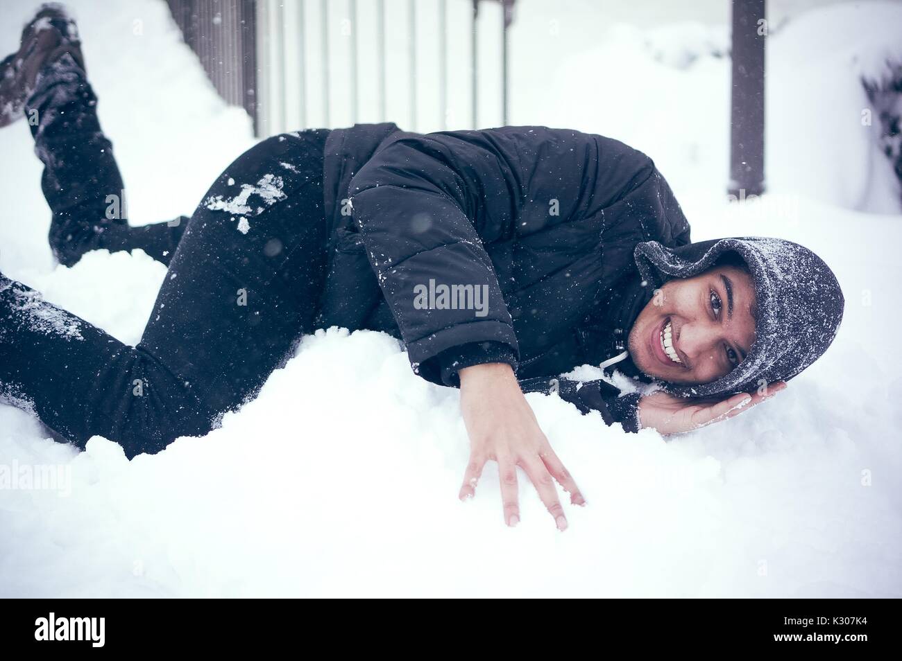 A student in hood and snow gear lays on a mound of snow while posing for his photo, on a snow day at Johns Hopkins University, Baltimore, Maryland, 2016. Stock Photo