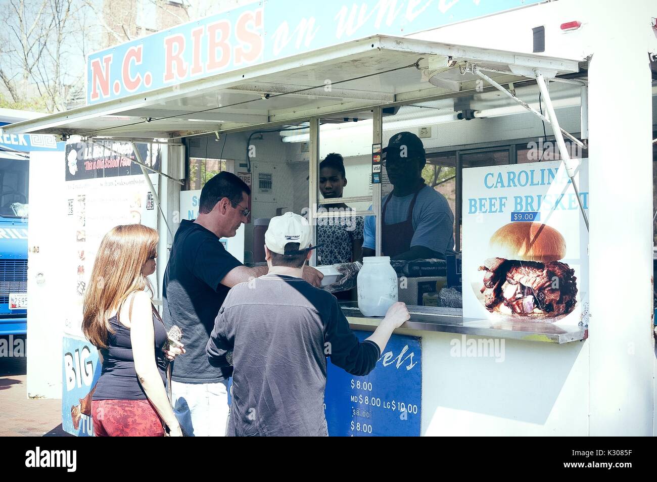 A woman and two men stand together ordering from a 'NC Ribs' food truck during Spring Fair, a student-run spring carnival at Johns Hopkins University, Baltimore, Maryland, April, 2016. Courtesy Eric Chen. Stock Photo