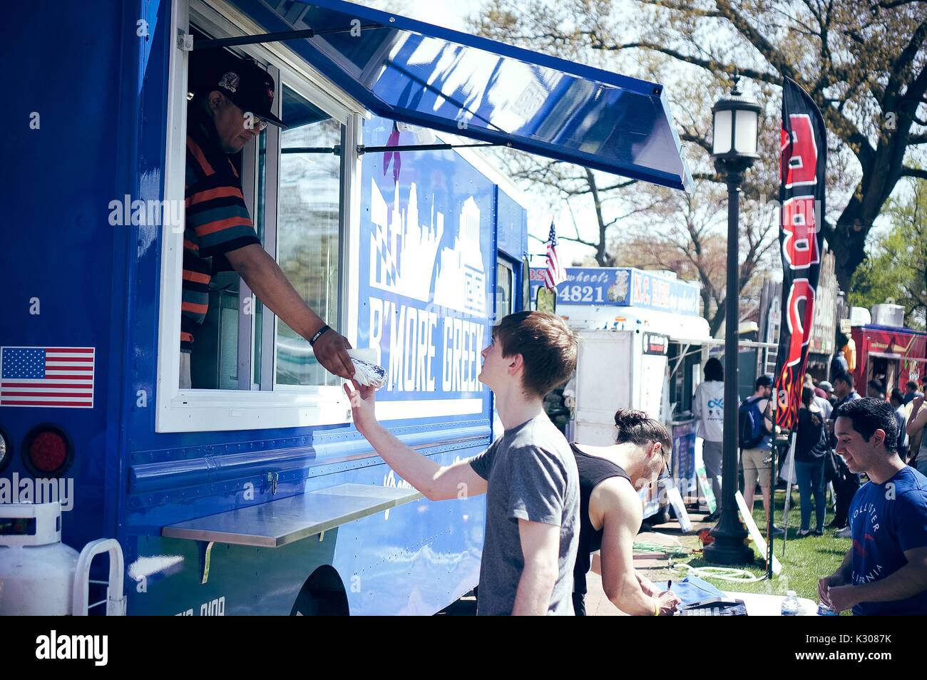 A man from inside a food truck hands a male student a sandwich wrapped in foil, during Spring Fair, a student-run spring carnival at Johns Hopkins University, Baltimore, Maryland, April, 2016. Courtesy Eric Chen. Stock Photo