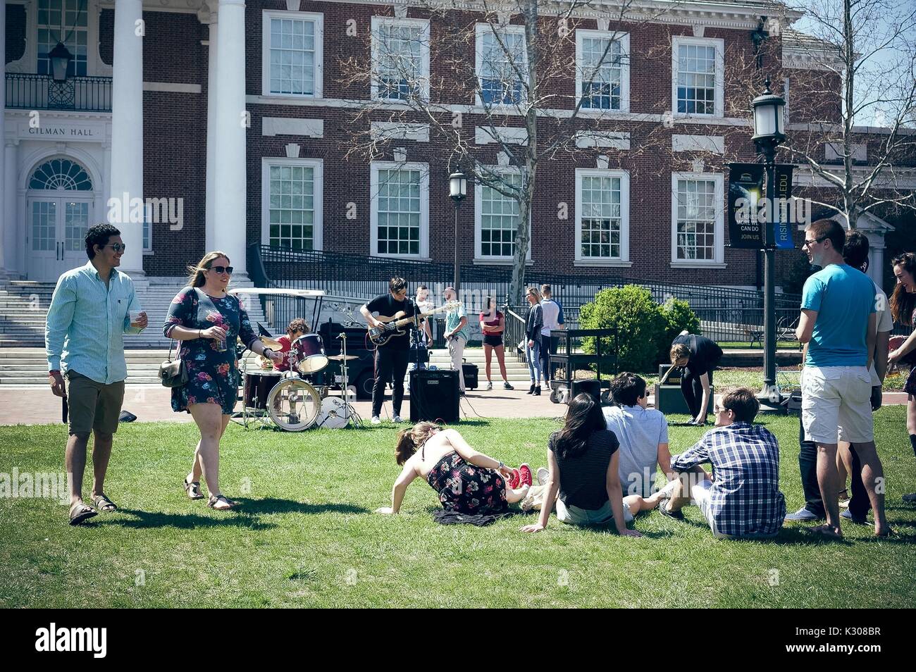 Students walk with drinks and sit on the grass to enjoy a student band playing in front of Gilman Hall, during Spring Fair, a student-run spring carnival at Johns Hopkins University, Baltimore, Maryland, April, 2016. Courtesy Eric Chen. Stock Photo