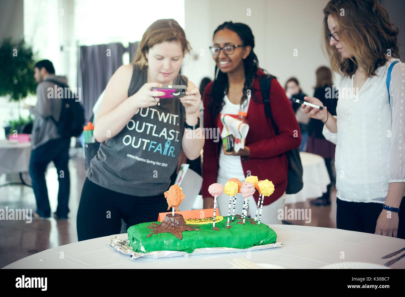 Undergraduate students taking pictures of a cake decorated for 'The Lorax' at the Edible Book Festival at Johns Hopkins University, Baltimore, Maryland, March 31, 2016. Courtesy Eric Chen. Stock Photo