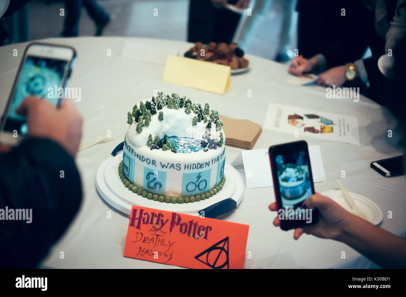 Undergraduate college students take pictures of a Harry Potter and the Deathly Hallows cake at the Johns Hopkins University's annual 'Read It And Eat It' Edible Book Festival on the Homewood campus in Baltimore, Maryland, March, 2016. Courtesy Eric Chen. Stock Photo