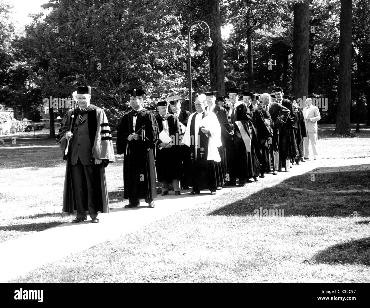 On Commencement Day, faculty wearing caps and gowns proceed in a line along a brick path