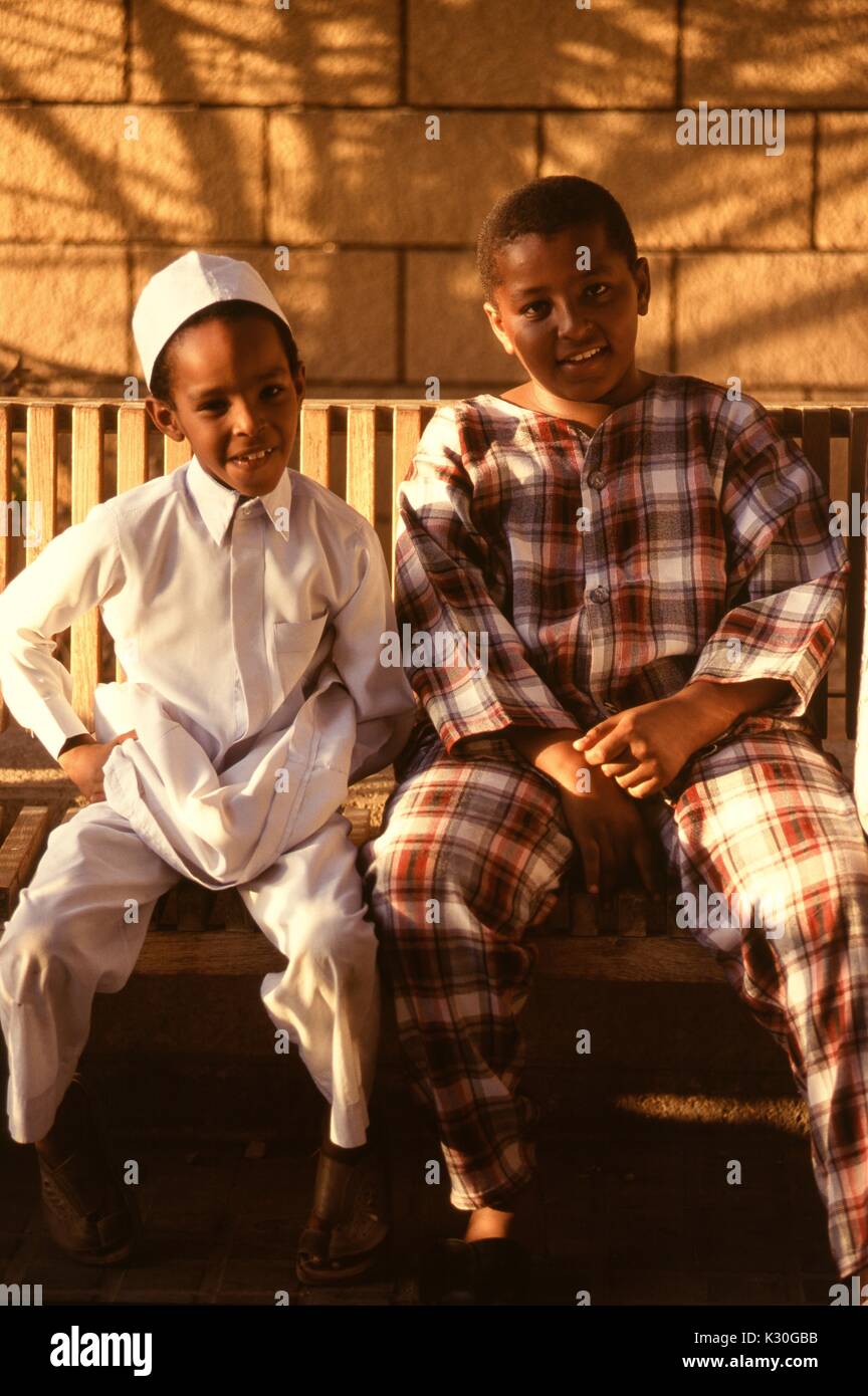 Two Saudi boys sitting on a wooden bench in Jeddah, by the red sea. Stock Photo