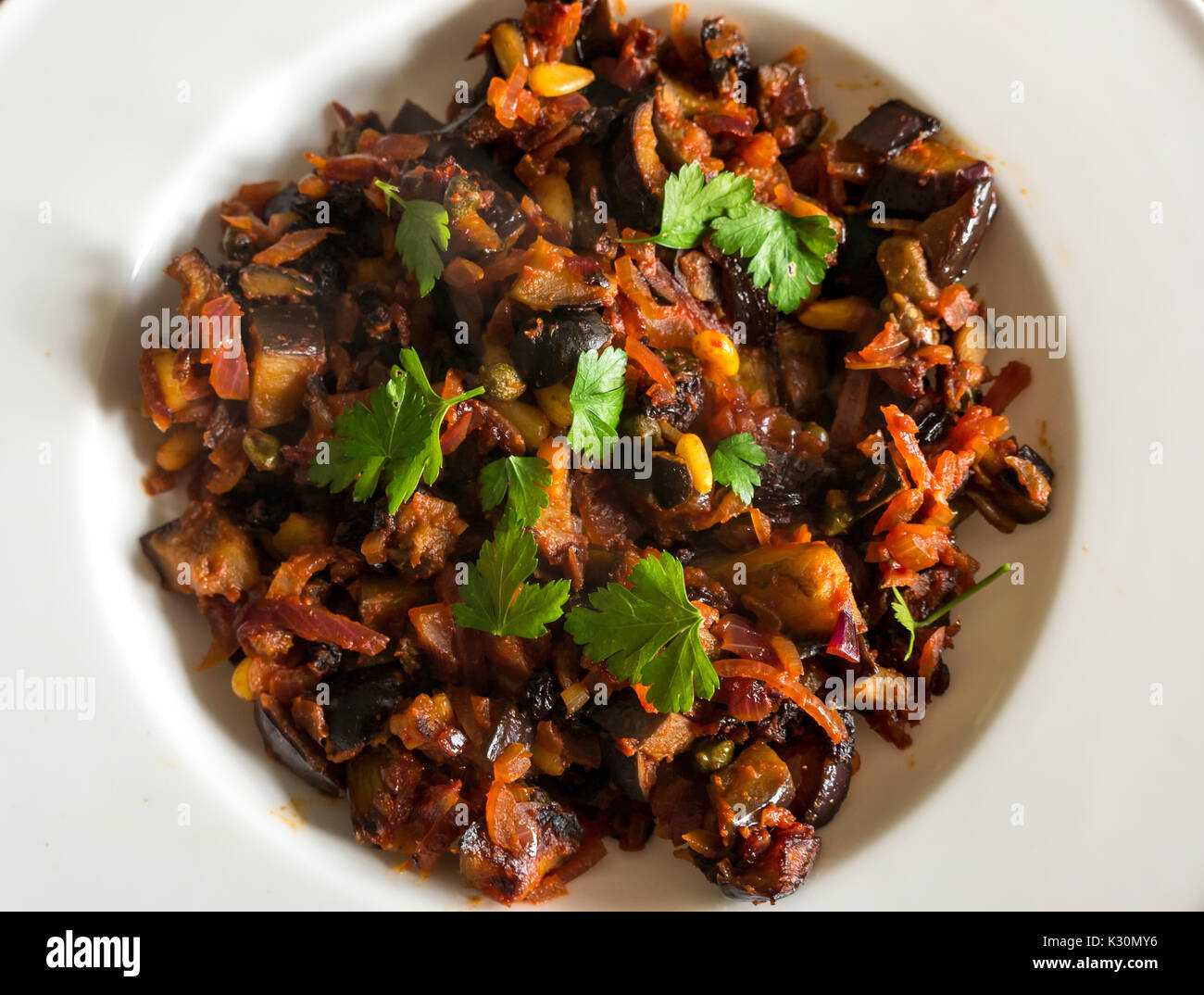 Close up of Sicilian dish, Caponata, with aubergine, olives, capers, red onion, pine kernels, tomato paste, served on a white plate Stock Photo