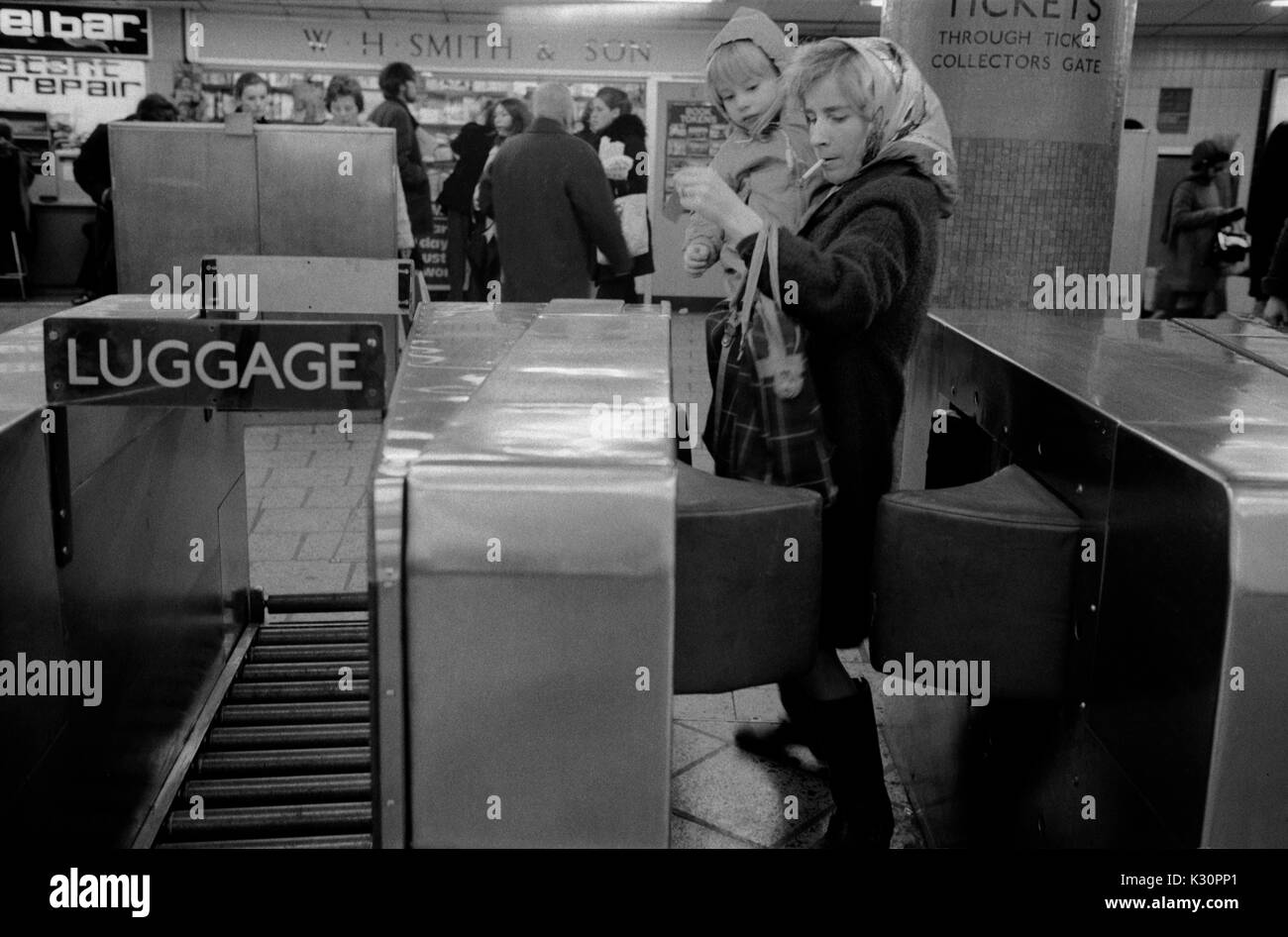 Underground tube train station new ticket barriers 1970s Mother and child, mum smoking carrying small child in her arms, 1975. UK HOMER SYKES Stock Photo