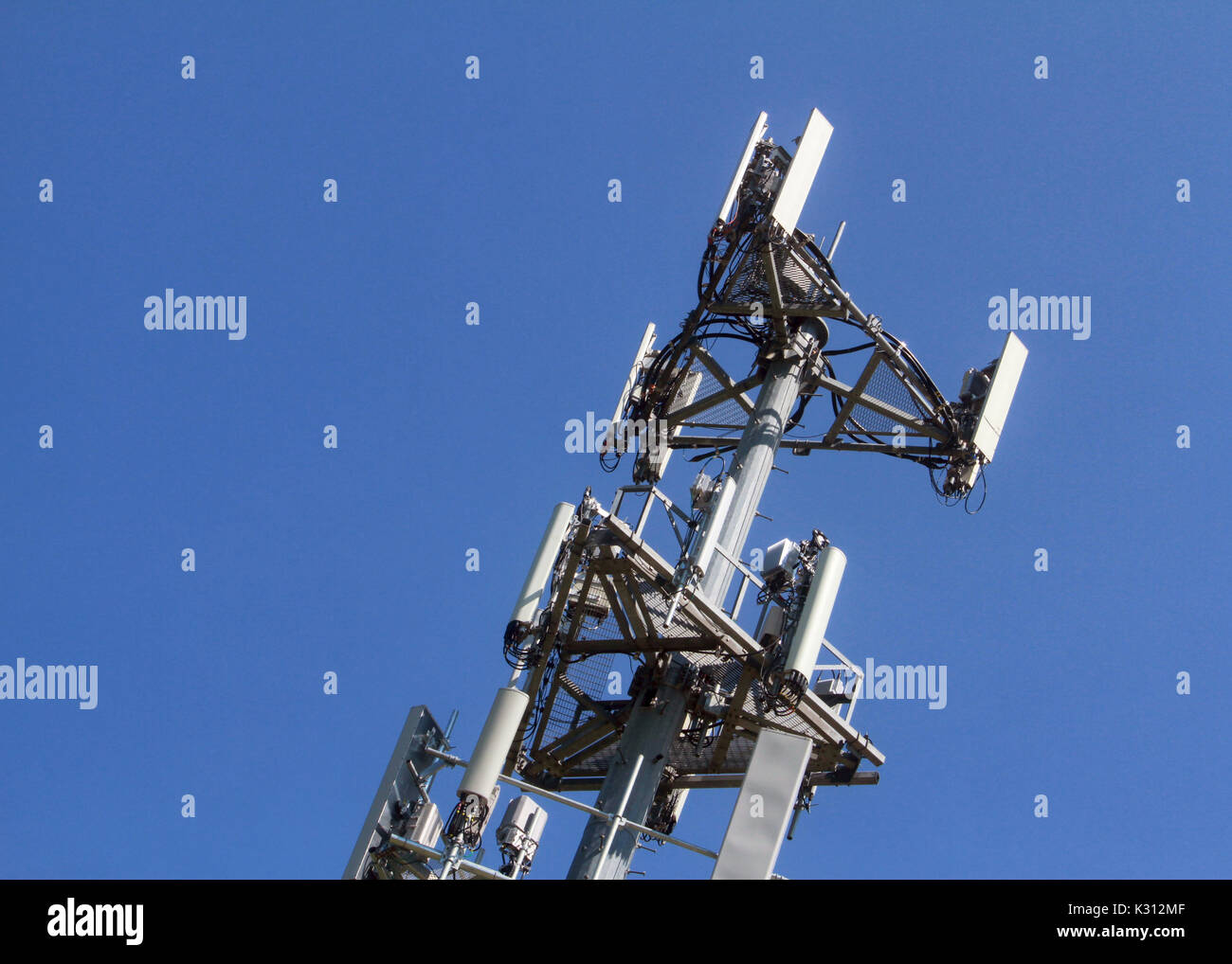 The top of a communications cellular tower stands out against a clear blue sky. Stock Photo
