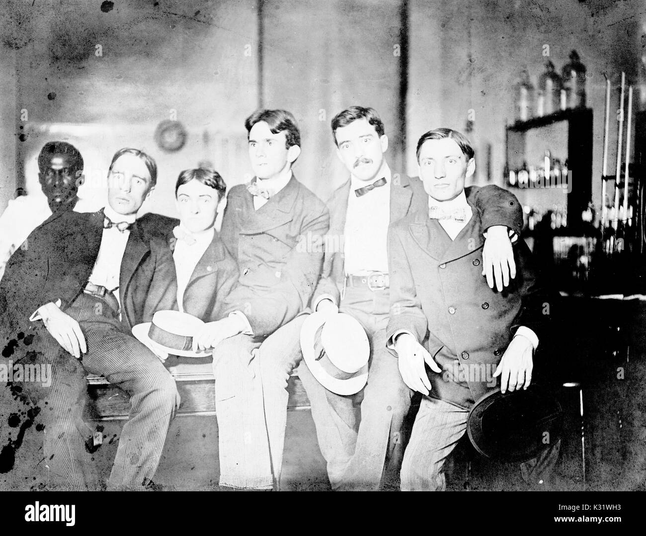 Group photograph of 1901 Johns Hopkins University PhDs in a laboratory, with arms on each others' shoulders, making funny facial expressions and holding skimmer hats, with one African-American man visible in the background, 1901. Stock Photo