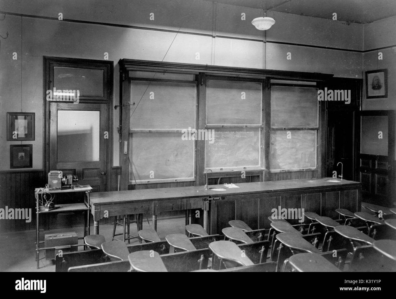 Sepia photograph of a third floor graduate lecture room inside the Chemistry Building at Old Campus Johns Hopkins University, showing rows of empty auditorium style desks facing the front of the classroom, with a blackboard covered in Organic Chemistry problems, Baltimore, Maryland, 1918. Stock Photo
