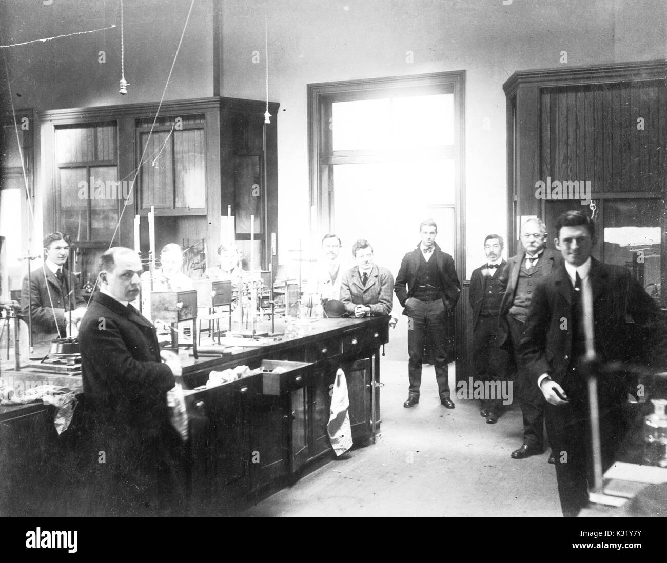 Photograph of the interior of the Harmon N Morse Chemical Laboratory at old campus Johns Hopkins University, featuring eight standing chemists from his lab clustered around benches with glassware and equipment, wearing suits, including Harmon Northrup Morse, Ira Obed Schaub, Benjamin Franklin Carver, John P Coony, Paul Edward Schaun, Howard Waters Doughty, Stanley DeVries Shipley, Rene de Mortemer Taveau, Isabura Wada, and John Hendricken King, Baltimore, Maryland, 1902. Stock Photo