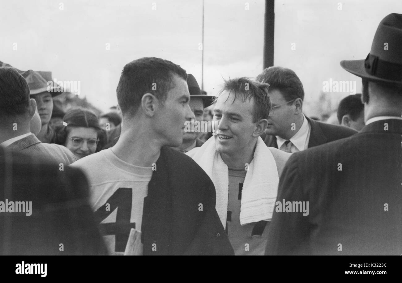Sepia tone candid photograph of co-captains of the men's lacrosse team at Johns Hopkins University, Byron Forbush and Joe Sollers, smile and look back at each other as they walk off the field, surrounded by fans and coaches, at the end of a victory against Loyola College, Baltimore, Maryland, June, 1951. Stock Photo