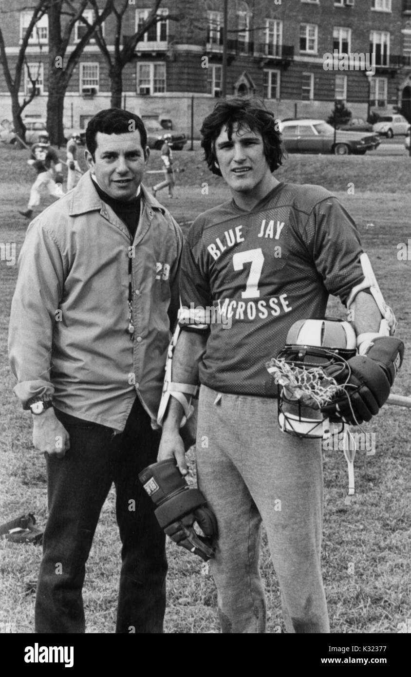 Grayscale portrait photograph of male lacrosse player for Johns Hopkins University, wearing a number 7 jersey and holding his gear, standing on the field next to head coach Henry Ciccarone, Baltimore, Maryland, 1978. Stock Photo