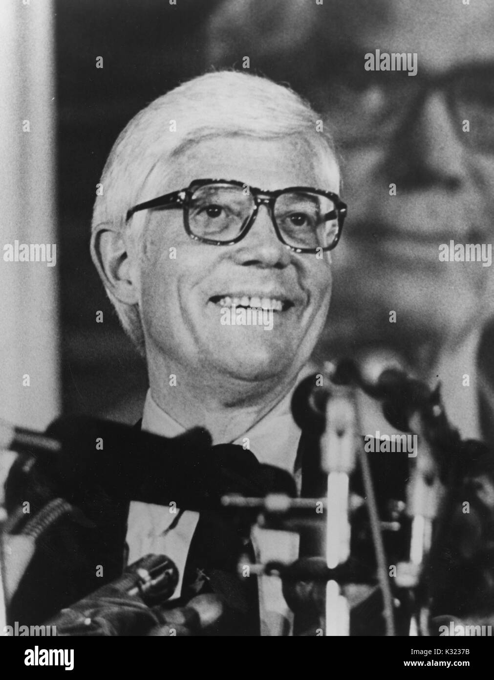 Grayscale portrait photograph, shoulders up, of US Representative John B Anderson of Illinois, smiling at a podium with numerous microphones in front of him, in attendance at the Milton S Eisenhower Symposium, a student-run annual speakers program at Johns Hopkins University, Baltimore, Maryland, 1980. Stock Photo