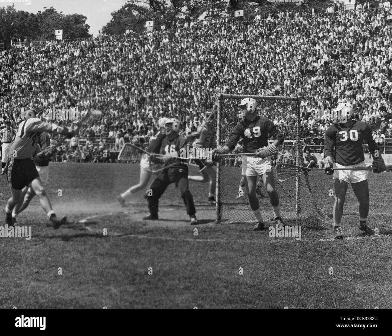 During a men's lacrosse game at Johns Hopkins University, a JHU player reaches to throw a powerful shot while members of the opposing team keep back for defense, in front of a sea of onlookers in the stands, Baltimore, Maryland, June, 1951. Stock Photo