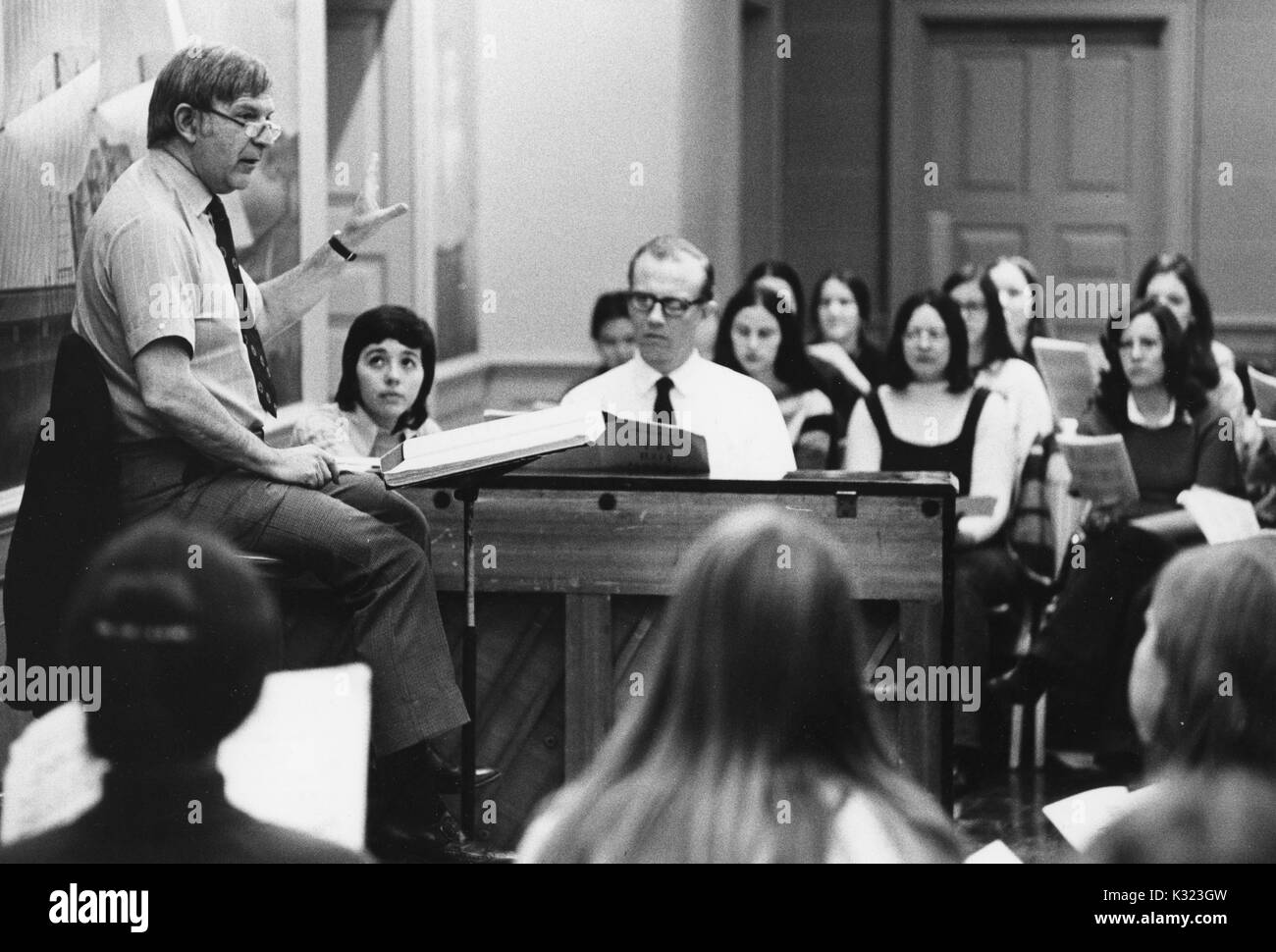 A choral director instructing his choir where adults are sitting holding their music books in front of them, 1980. Stock Photo