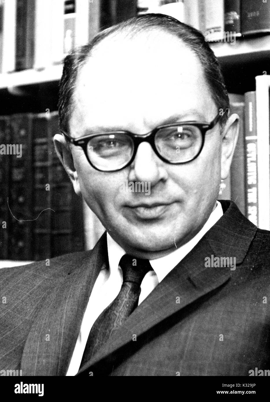 Portrait photograph of American historian and biographer David Herbert Donald sitting in front of bookshelves, 1962. Stock Photo