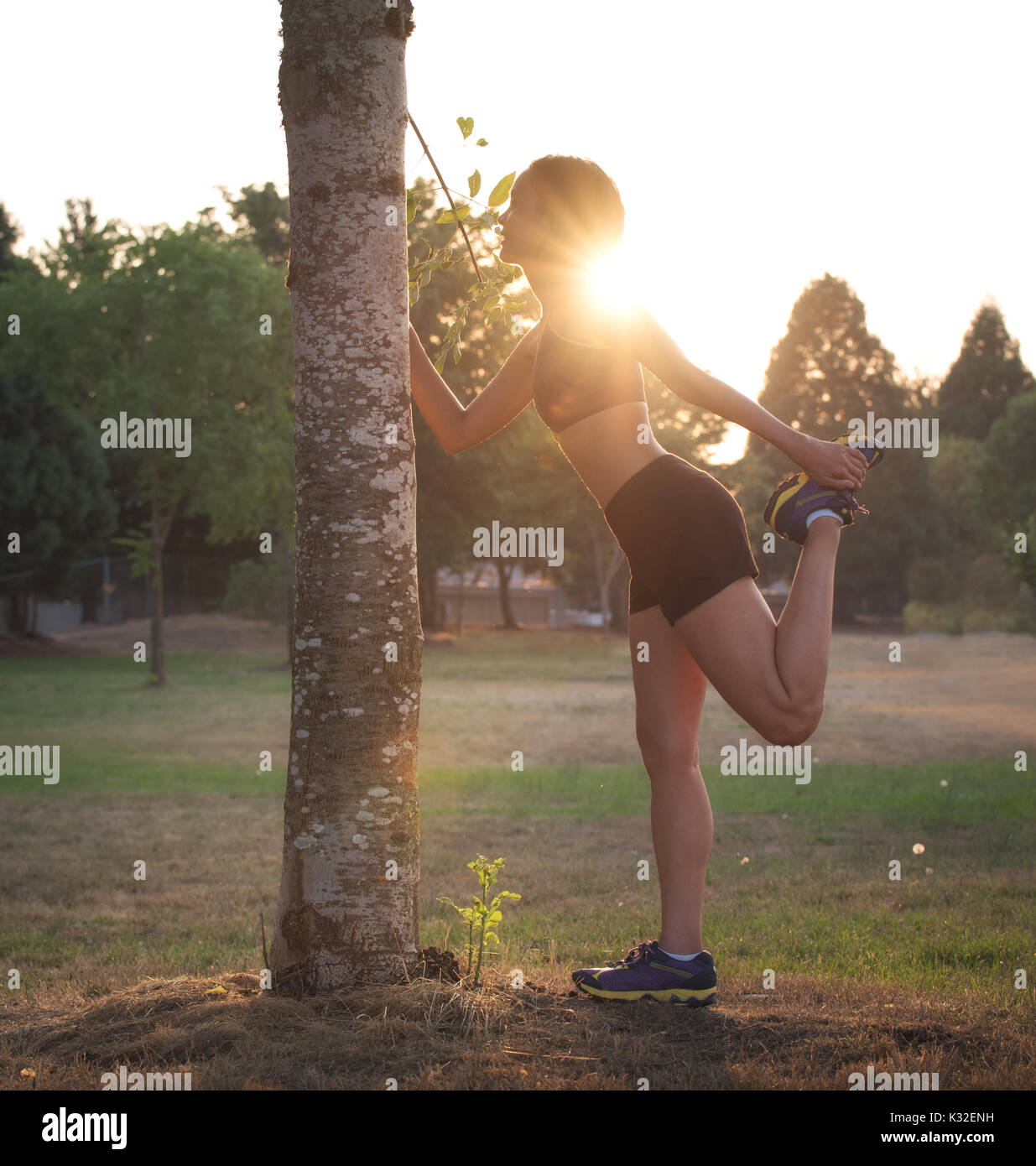 A female runner stretches her legs at sunset in a park. Stock Photo