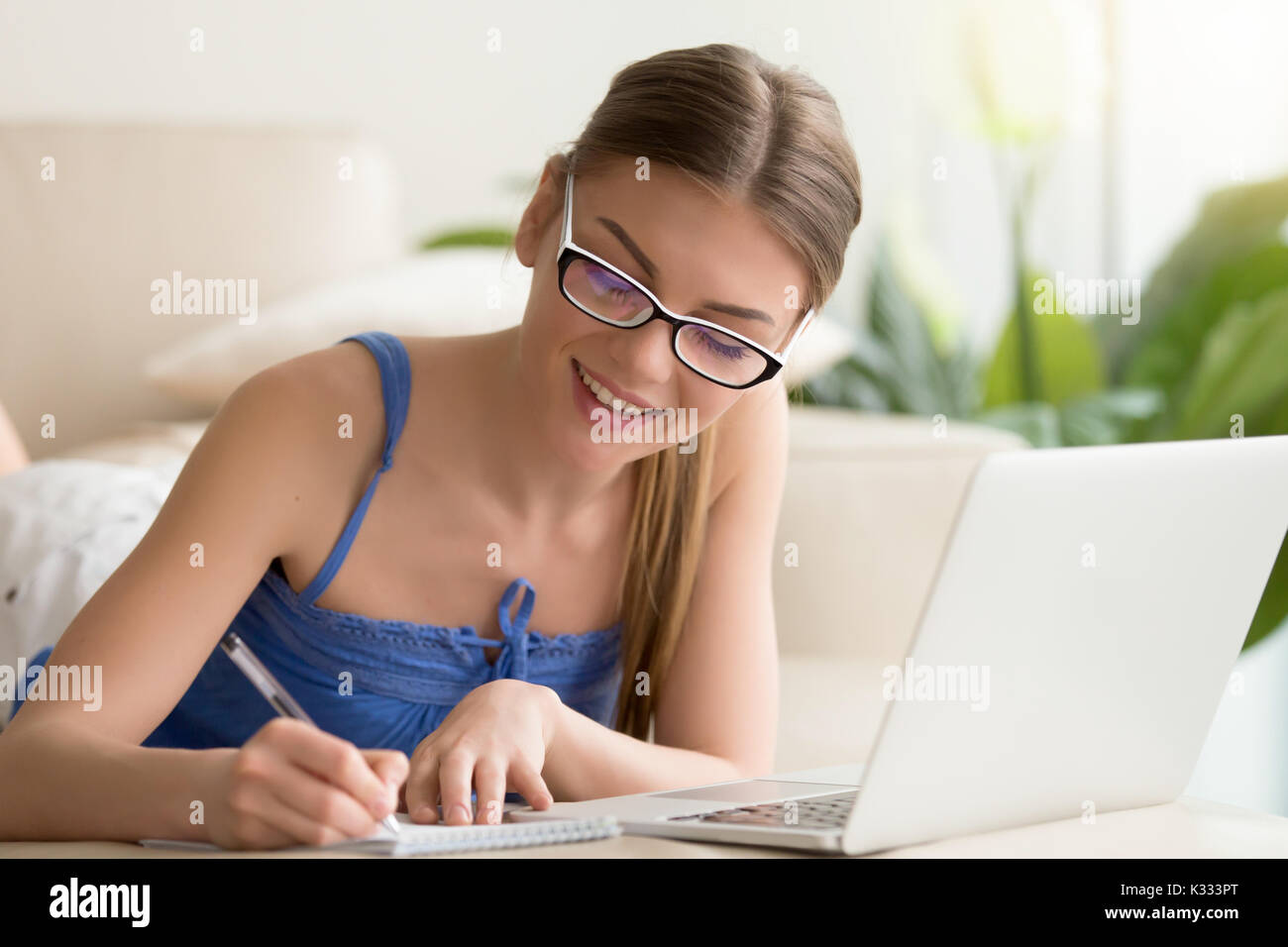 Lady writing in notebook when using laptop at home Stock Photo