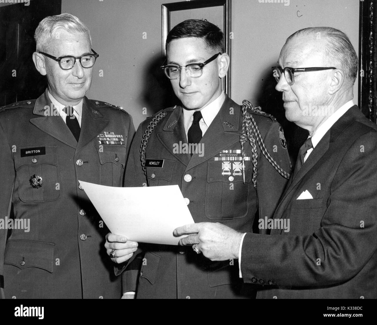 Milton Stover Eisenhower, President of Johns Hopkins University, stands to present the Distinguished Military Student Award to James Hemsley, wearing uniform and holding paper certificate, next to Major General Frank H Britten in uniform to his right, all three men wearing glasses, Baltimore, Maryland, 1965. Stock Photo