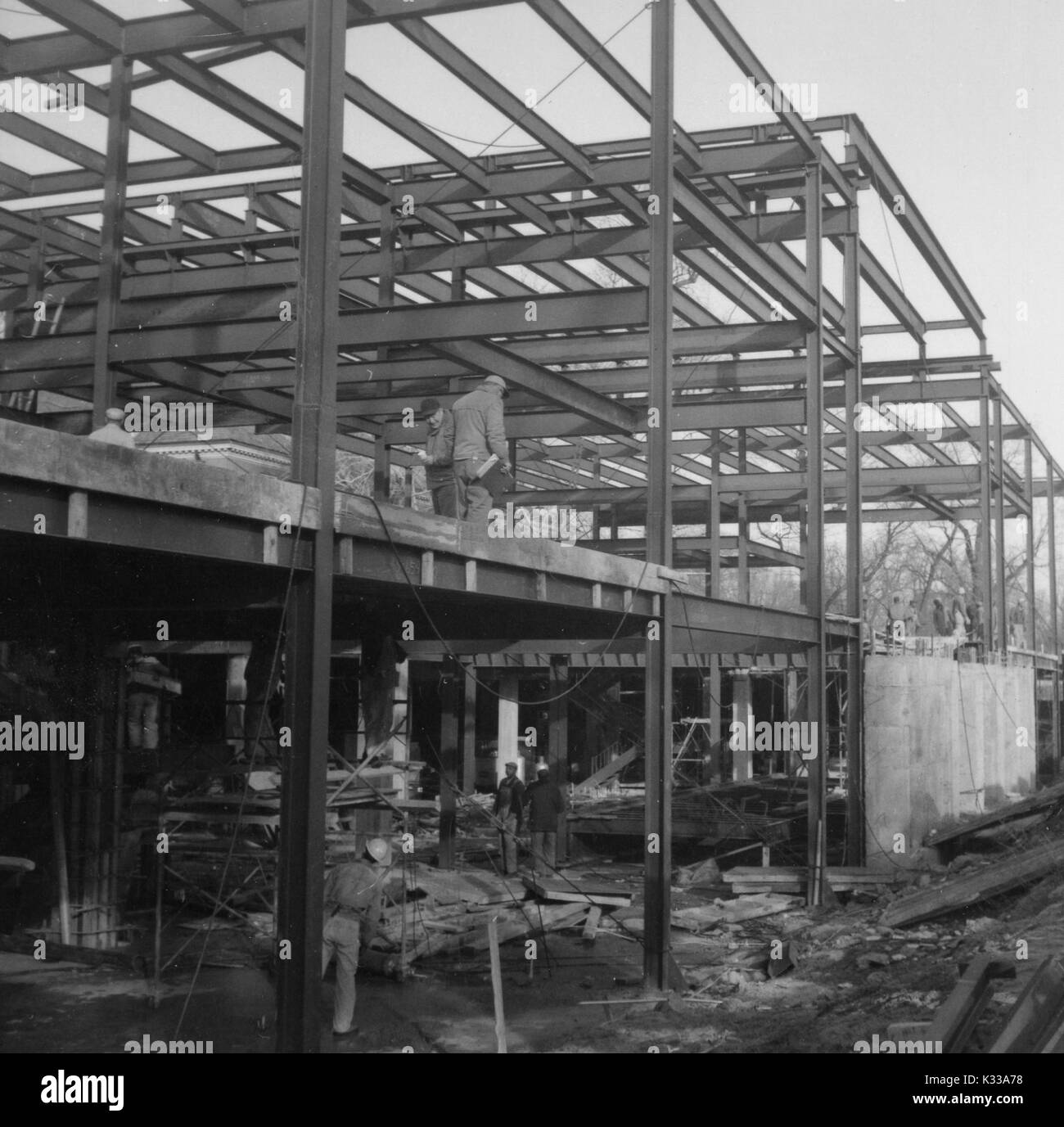 During the early stages of construction of the Milton S Eisenhower Library at Johns Hopkins University, workers stand on different levels made of stacked steel beams, the levels which will become Q and M floors of the library, above a construction site littered with rocks and boards and beams, Baltimore, Maryland, 1963. Stock Photo