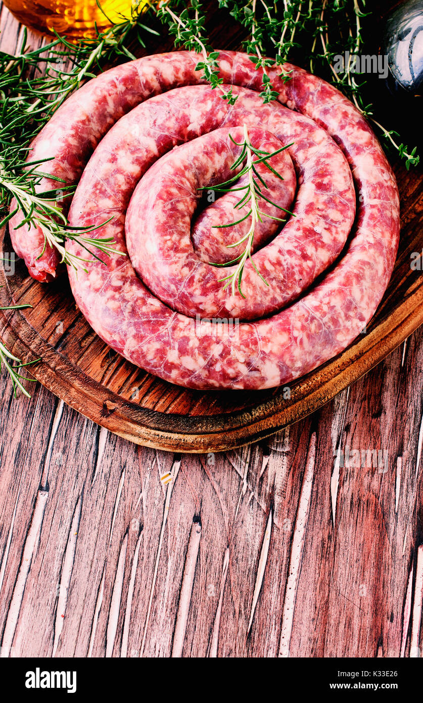 raw beef sausages on a cast-iron pan with rosemary and spices on a wooden table, South African boerewors Stock Photo