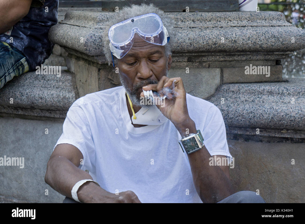 A man smoking three cigarettes at a time while wearing goggles and a face mask, In lower Manhattan, New York Ciy Stock Photo