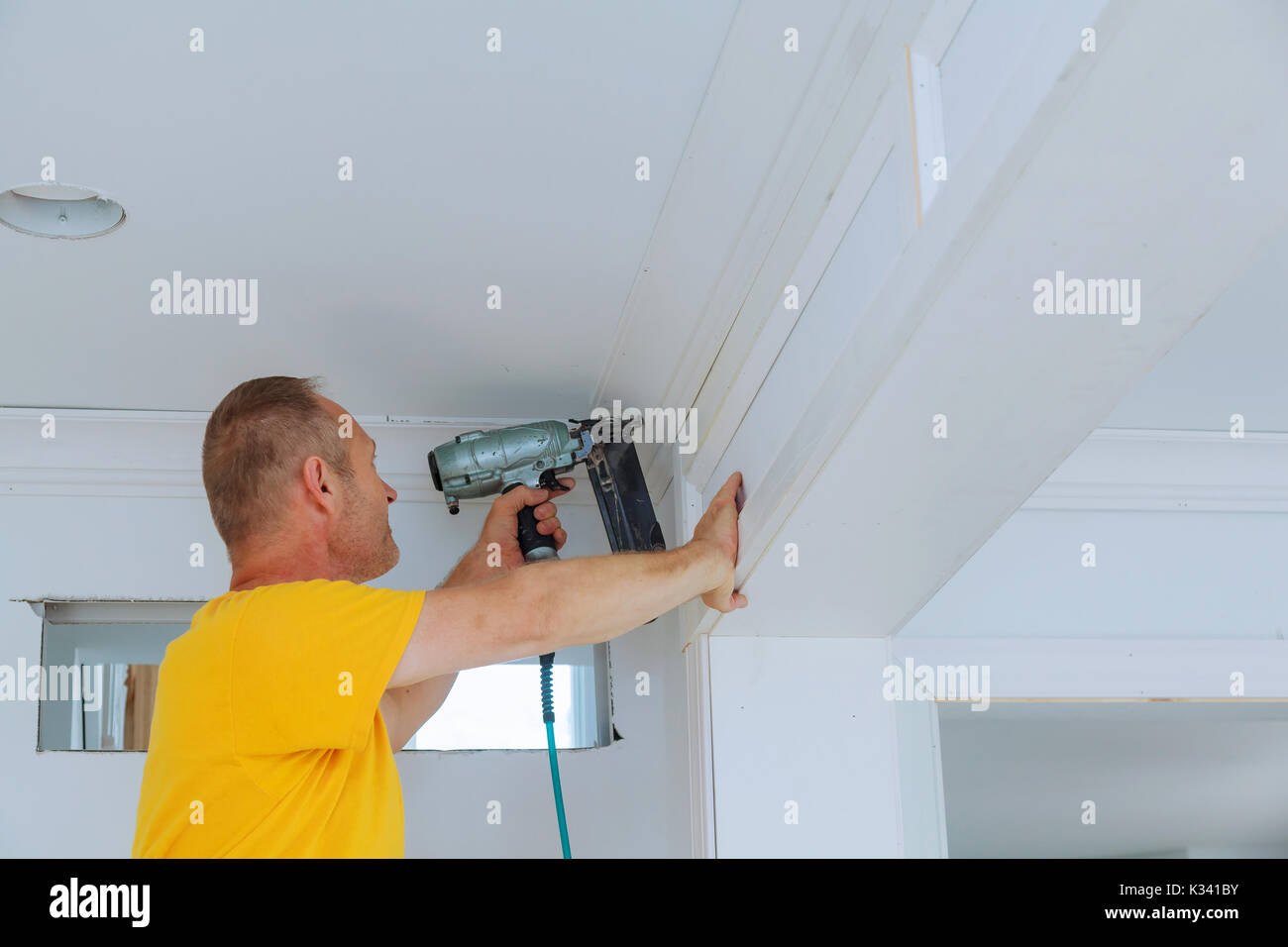 Carpenter brad using nail gun to Crown Moulding framing trim, with the