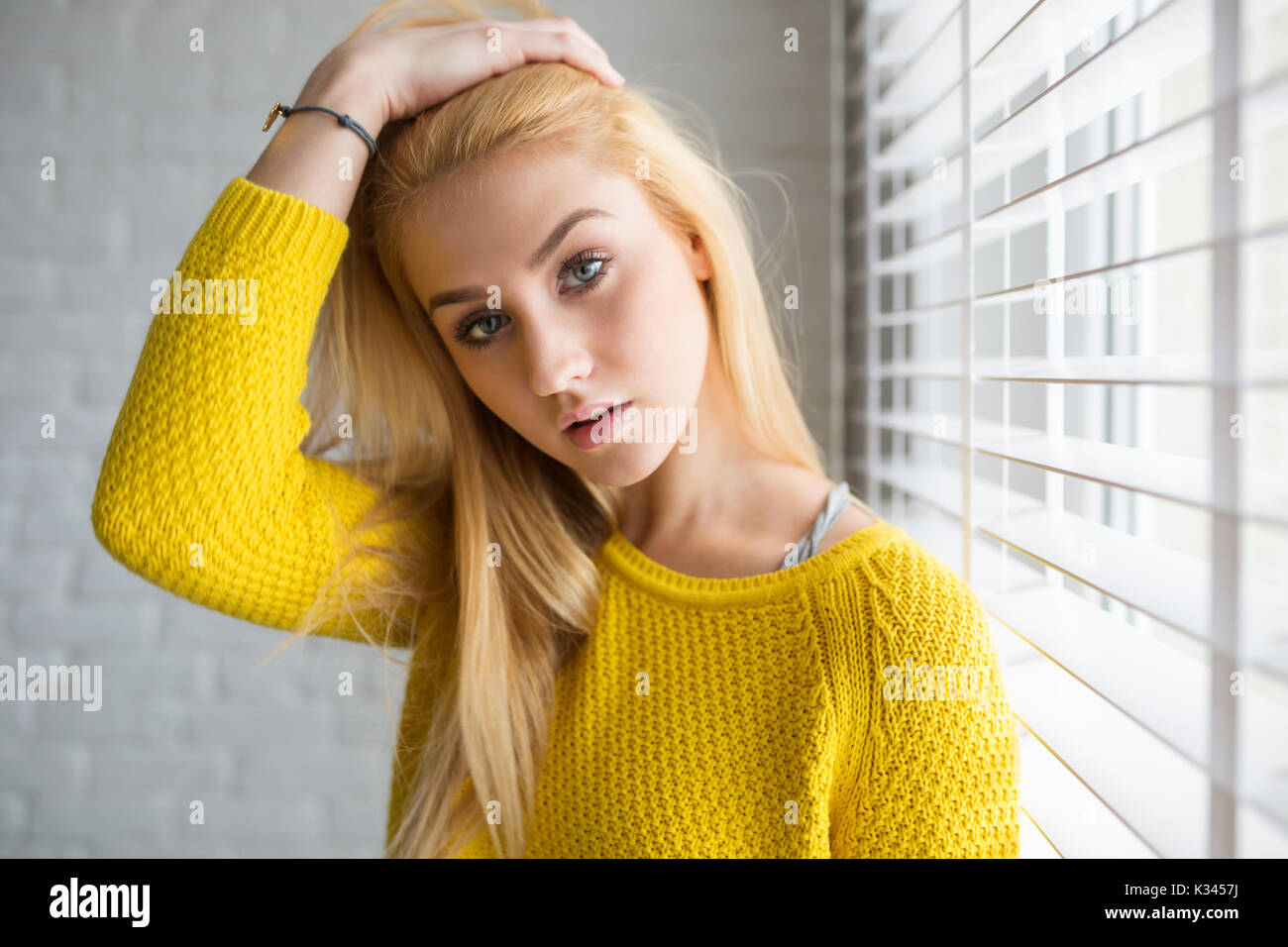 A Photo Of Young Woman Standing In Sensual Pose Brushing Aside Her Hair She S Wearing Yellow Sweater Stock Photo Alamy