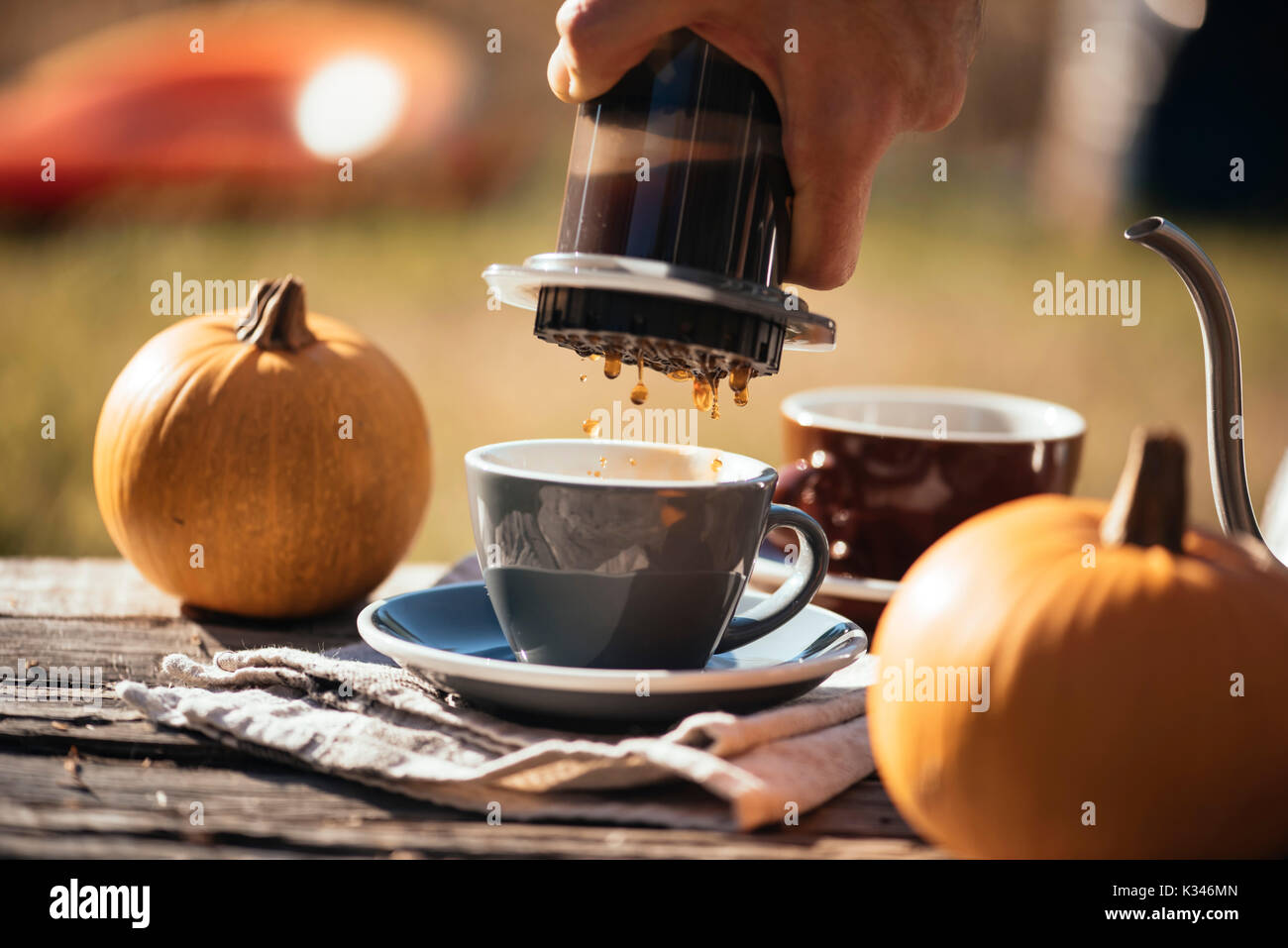 Man brewing filter coffee outdoor, at the autumn coffee picnic, on the old damaged wooden table background. Coffee drips captured in motion in the pro Stock Photo