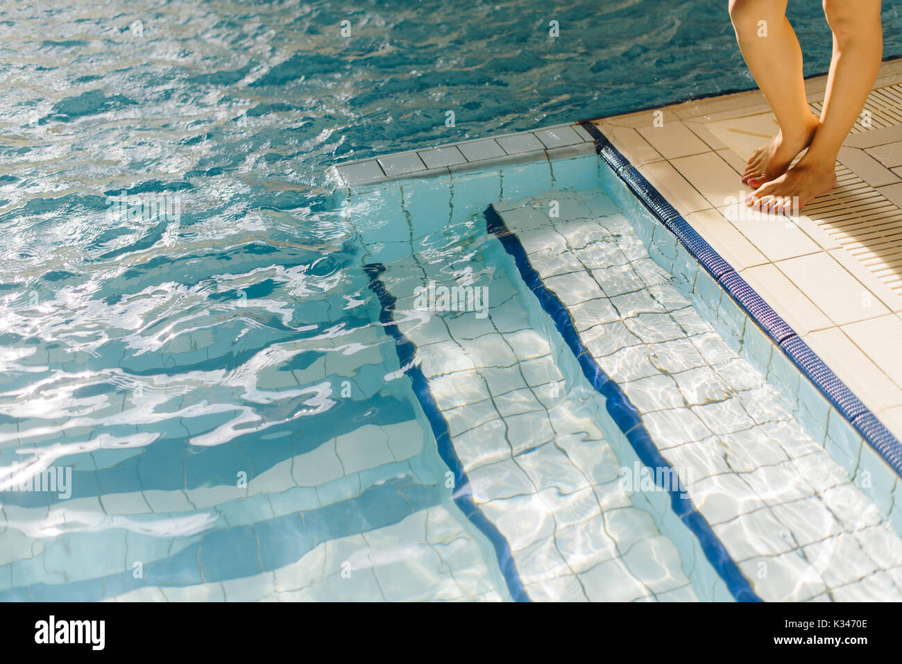 Young Woman Legs Standing On The Edge Of A Swimming Pool Dipping Her Legs In It On A Summer