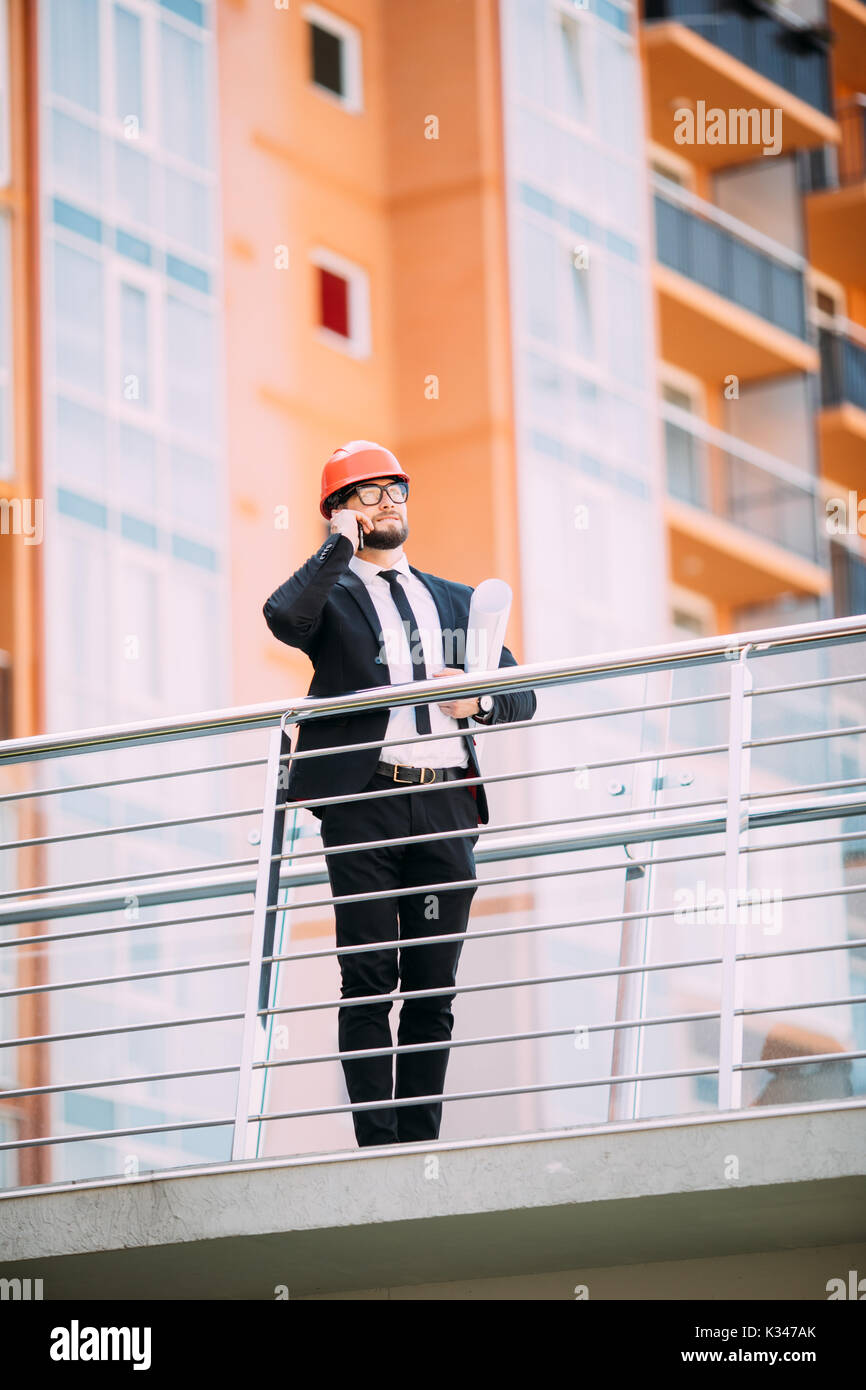 Engineer with plan in his hand talking on cell phone on construction building side. Stock Photo