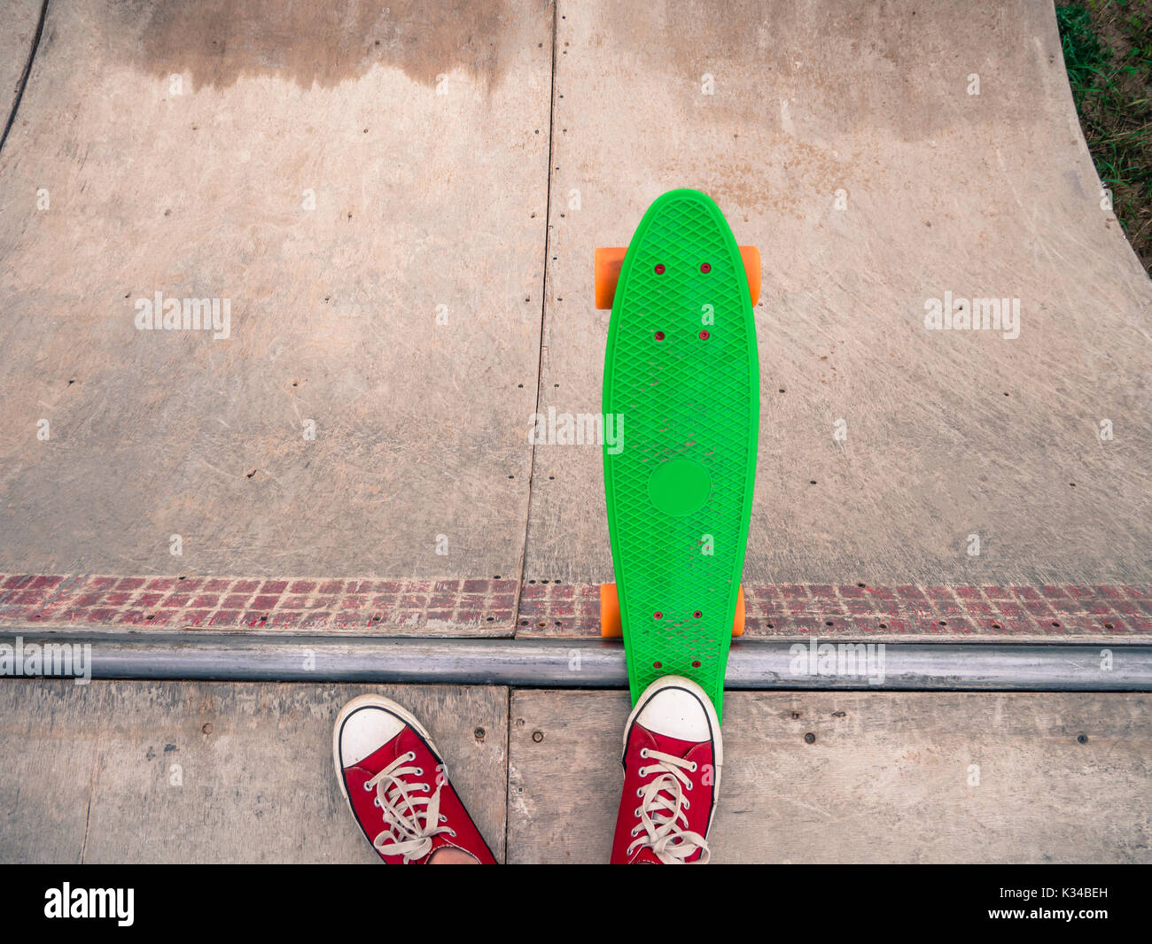 Low section of a male skater in red sneakers with a green penny board on the half-pipe. Stock Photo