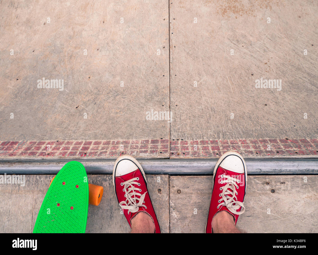 Low section of a male skater in red sneakers with a green penny board on the half-pipe. Stock Photo