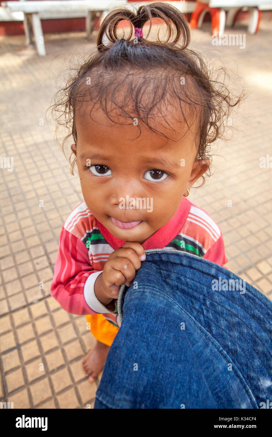 A cute young child with a blue hat and imploring eyes begs on a sidewalk in Siem Reap, Cambodia. Stock Photo