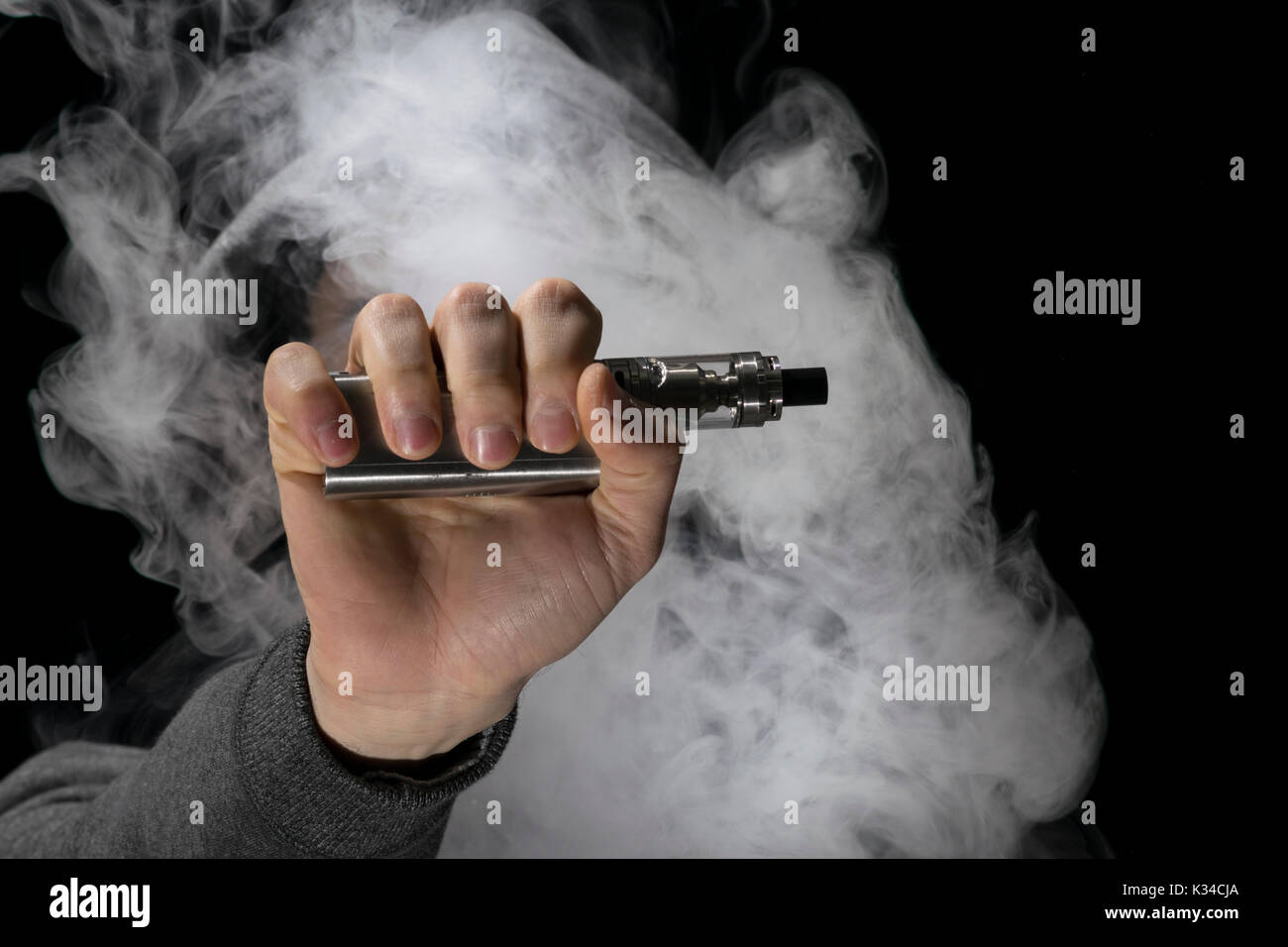 young man vaping electronic cigarette, holding a vape device with ...
