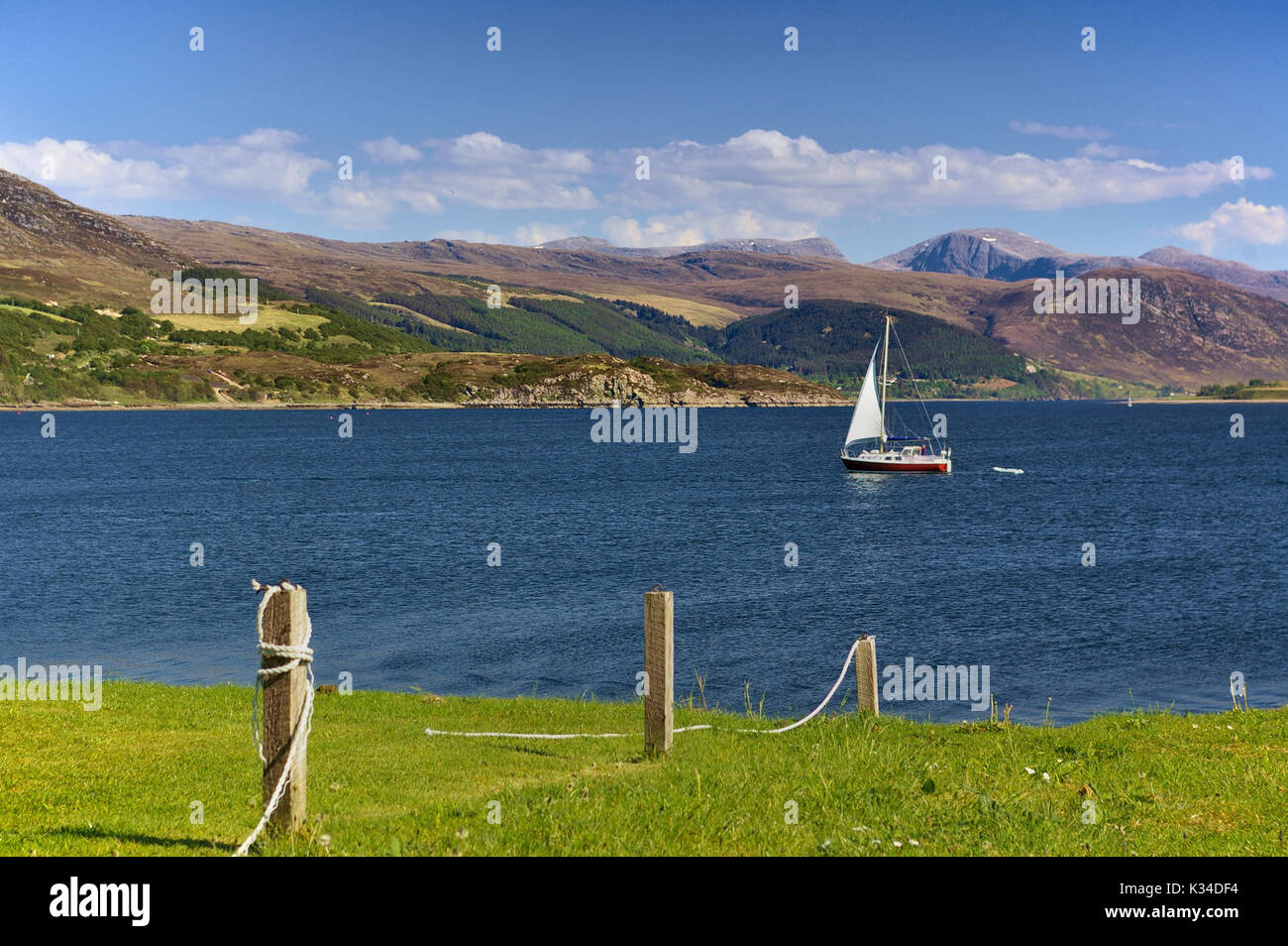 Sailing yacht at sea with mountain range in the background and green grassy seashore in the foreground, Ullapool, Wester Ross, Scotland Stock Photo
