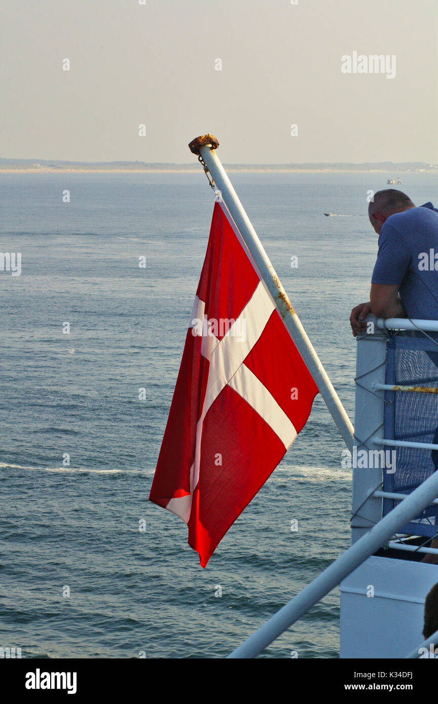 Danish flag hoisted on the flagpole of a ferry in the evening with the calm sea in the background Stock Photo