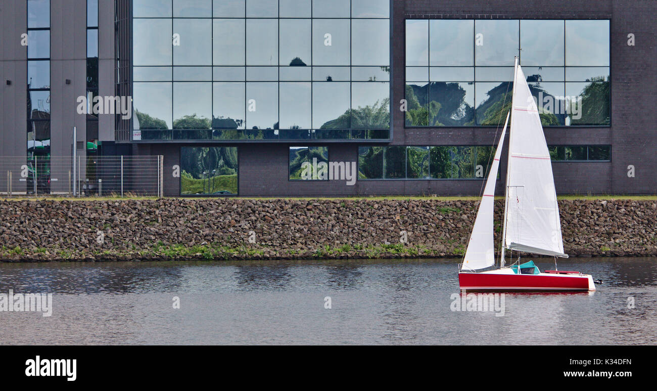 Red sailboat sailing past a waterfront office building Stock Photo Alamy